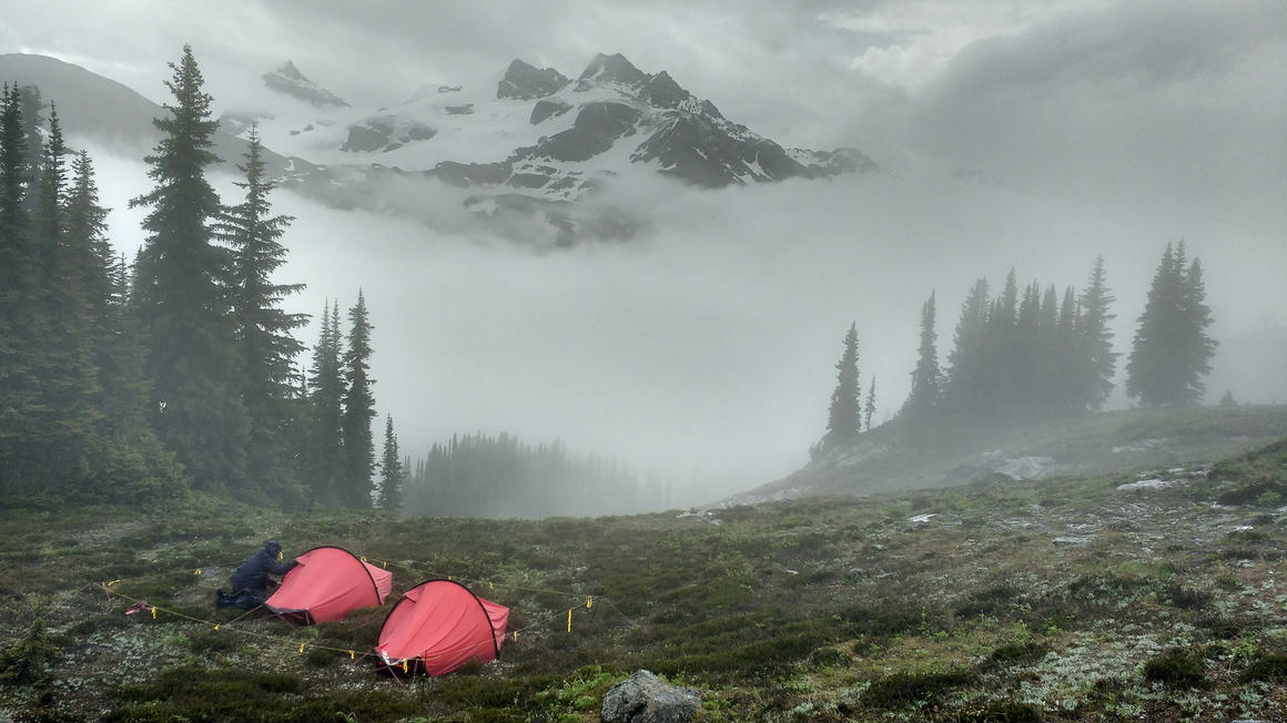 Our two red tents in a misty alpine setting with a figure seated, capturing the moody essence of the Canadian Rockies during rainy weather