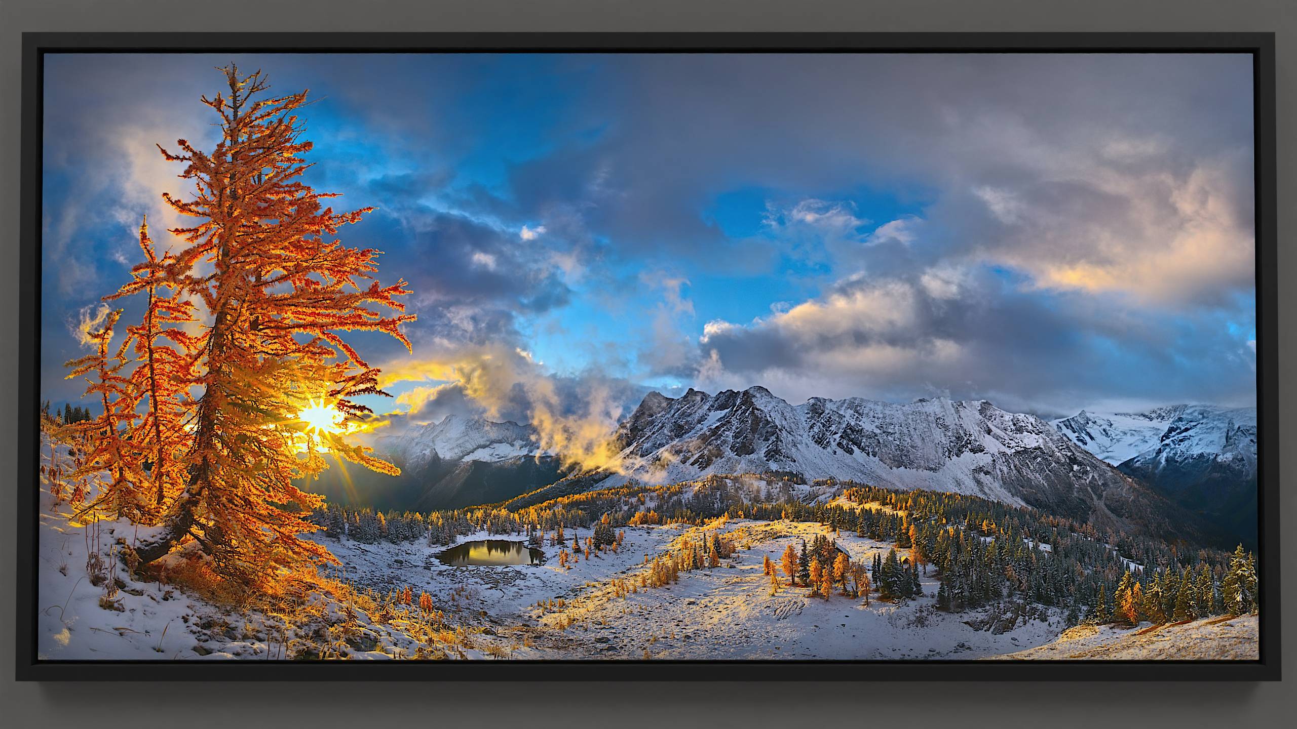 On a crisp morning at Jumbo Pass, golden larches glow under a cloud-swirled sky. Fresh snow adorns the hillside, casting playful shadows around Jumbo cabin on the pass. Beyond, Bastille mountain and Horseshoe glacier linger in blue shadow, embodying the simple, timeless elegance of the Purcell wilderness.